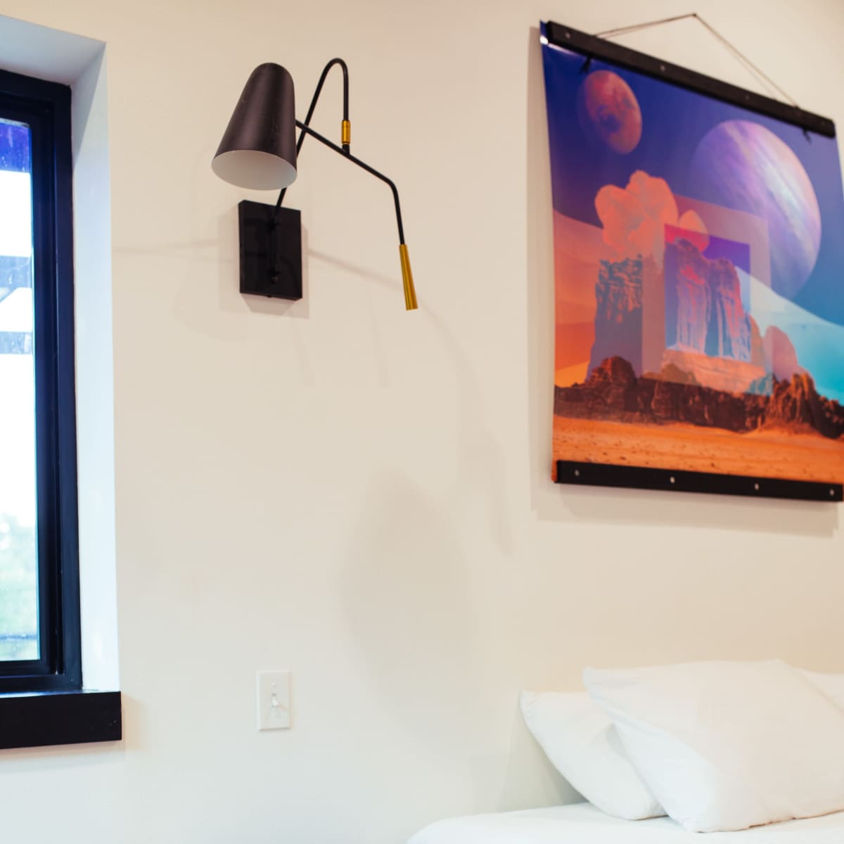 A minimalist bedroom featuring a bed with white bedding, a small nightstand with a remote, and a colorful abstract artwork on the wall above it.