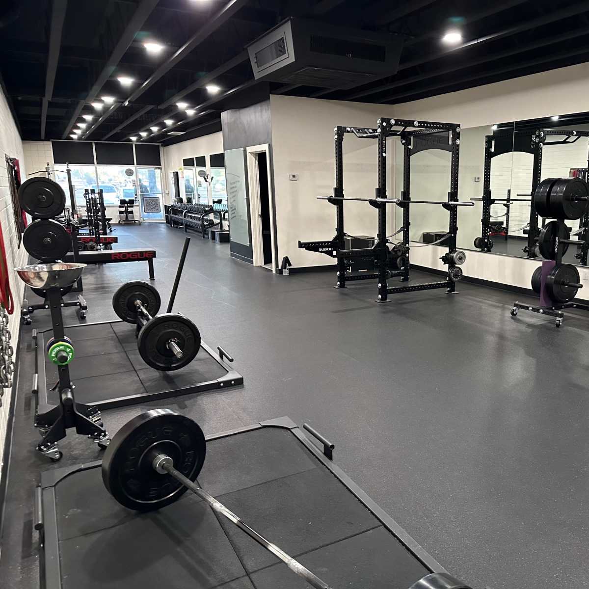 A modern gym interior with weightlifting equipment, including barbells and squat racks, set on a rubberized floor.