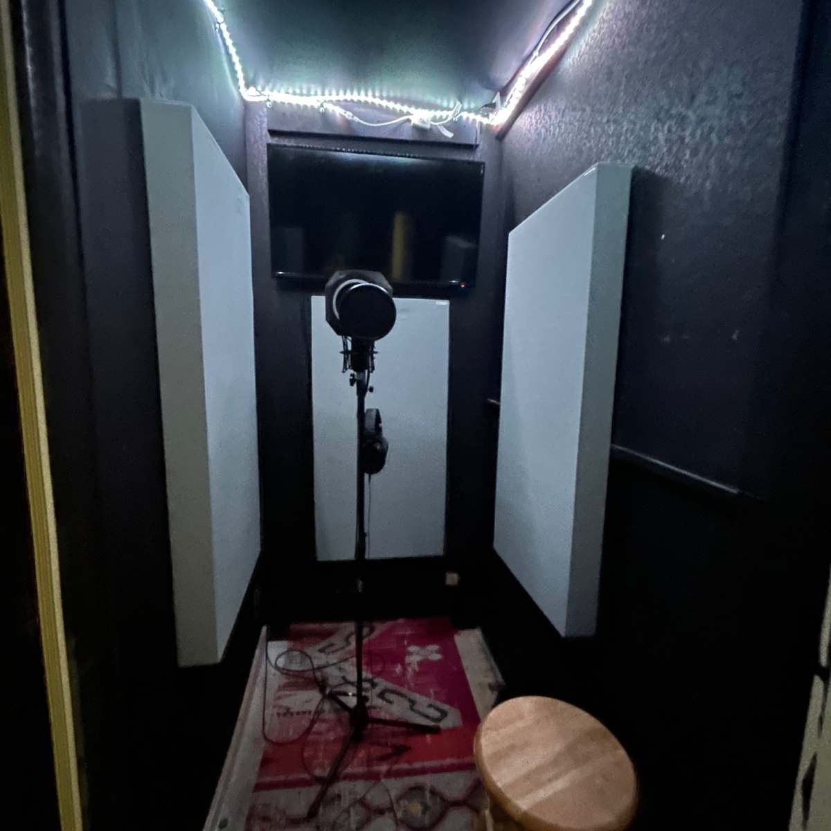 A small recording booth with soundproofing panels, a microphone on a stand, and a stool in the center.