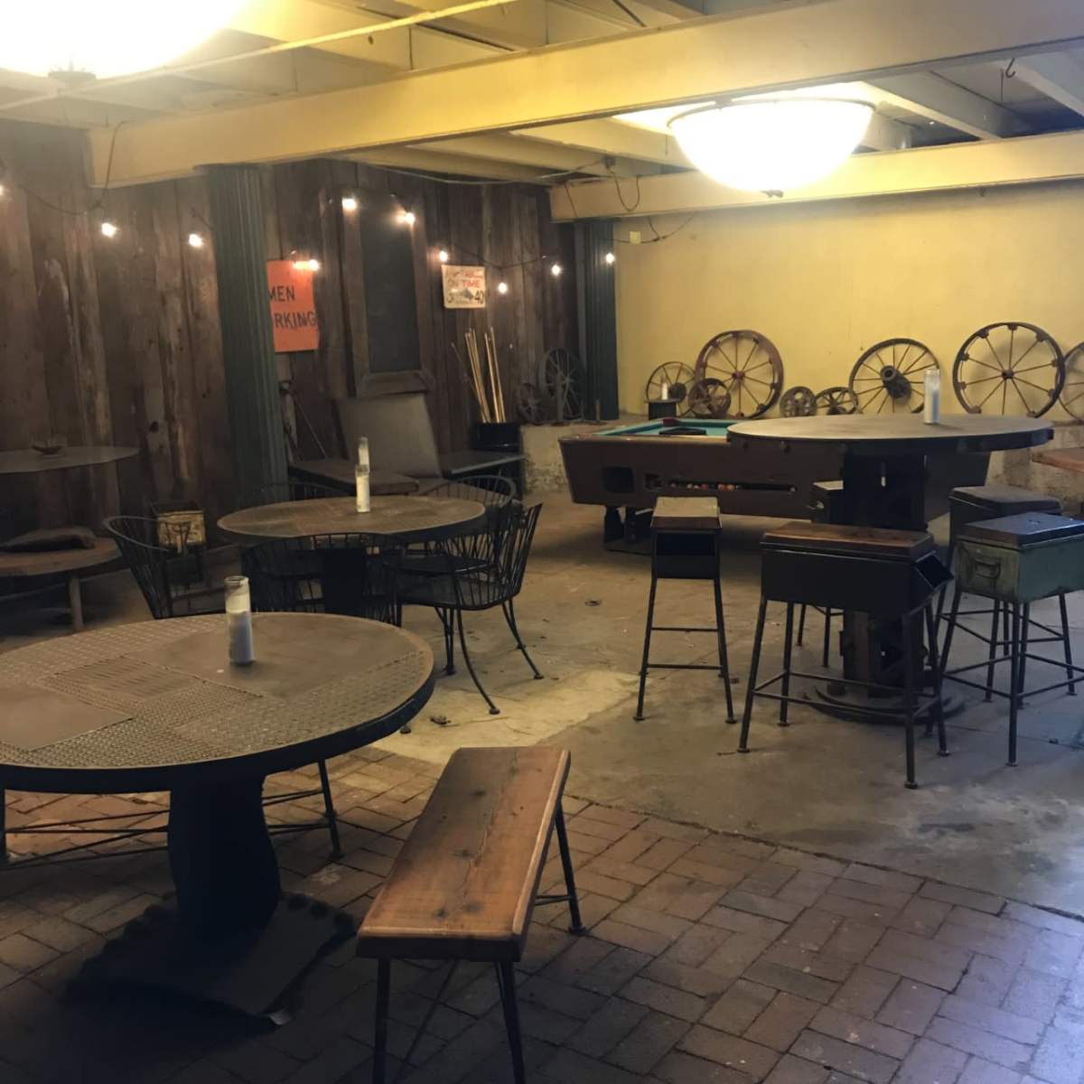 An indoor space with metal tables, wooden seating, and rustic decor, including vintage wheels against the walls.