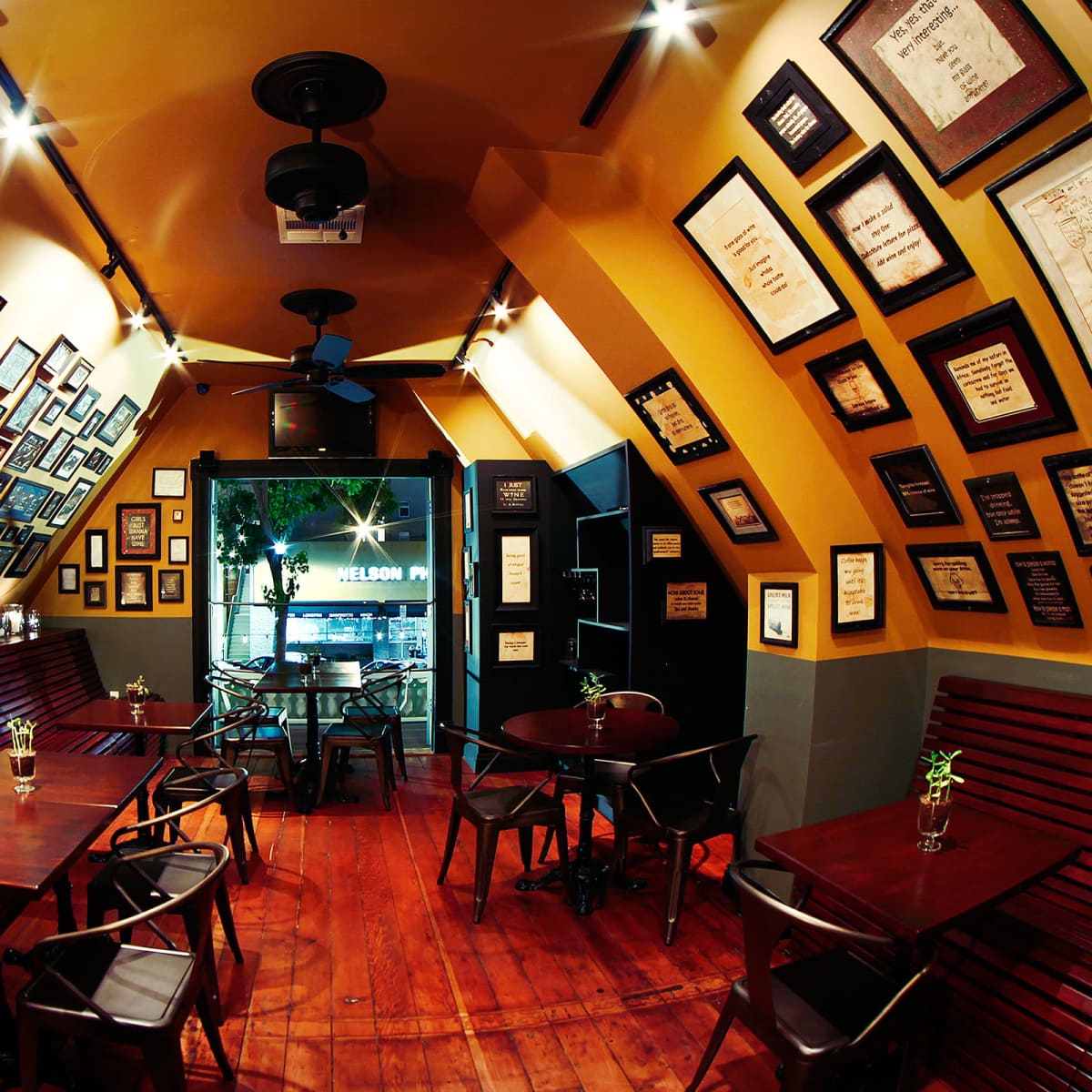 A small, cozy café with angled walls adorned with various framed pictures and certificates, featuring wooden tables and chairs arranged neatly.