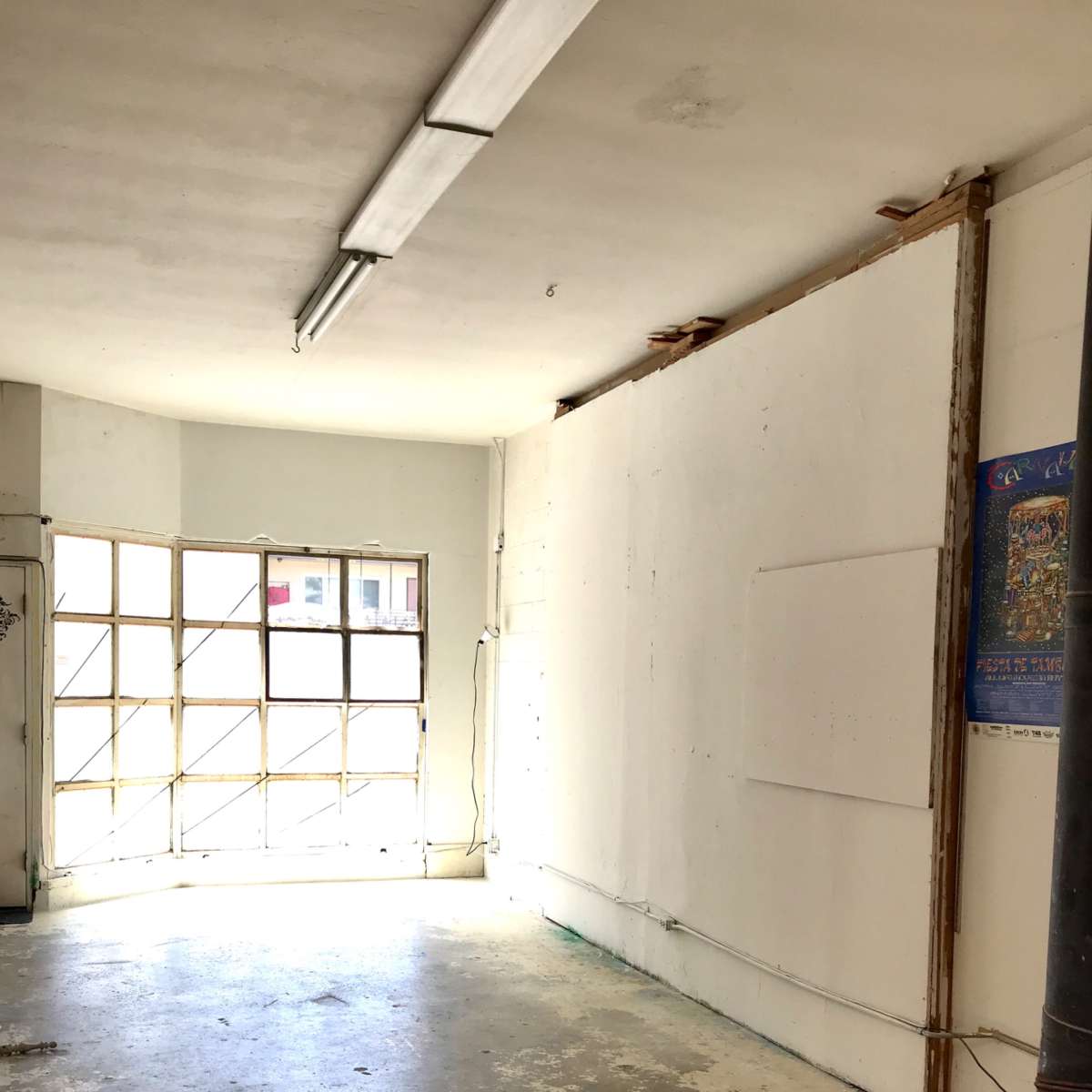 An empty room with a concrete floor, a large window letting in light, and bare white walls.