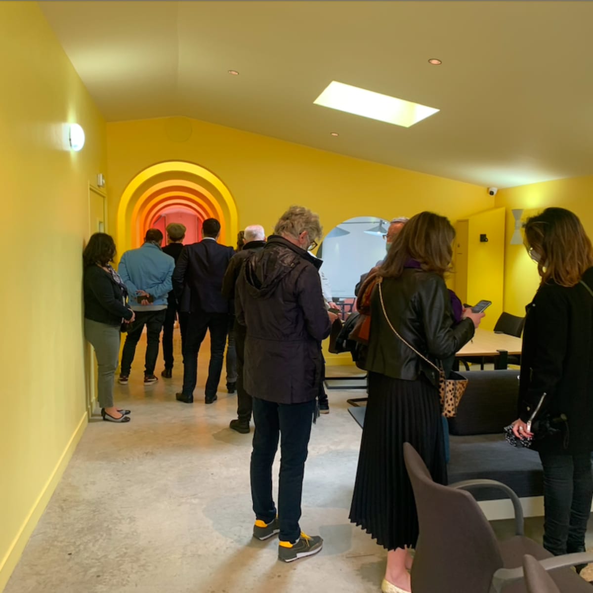 A group of people stands in a yellow hallway leading to a brightly lit archway.