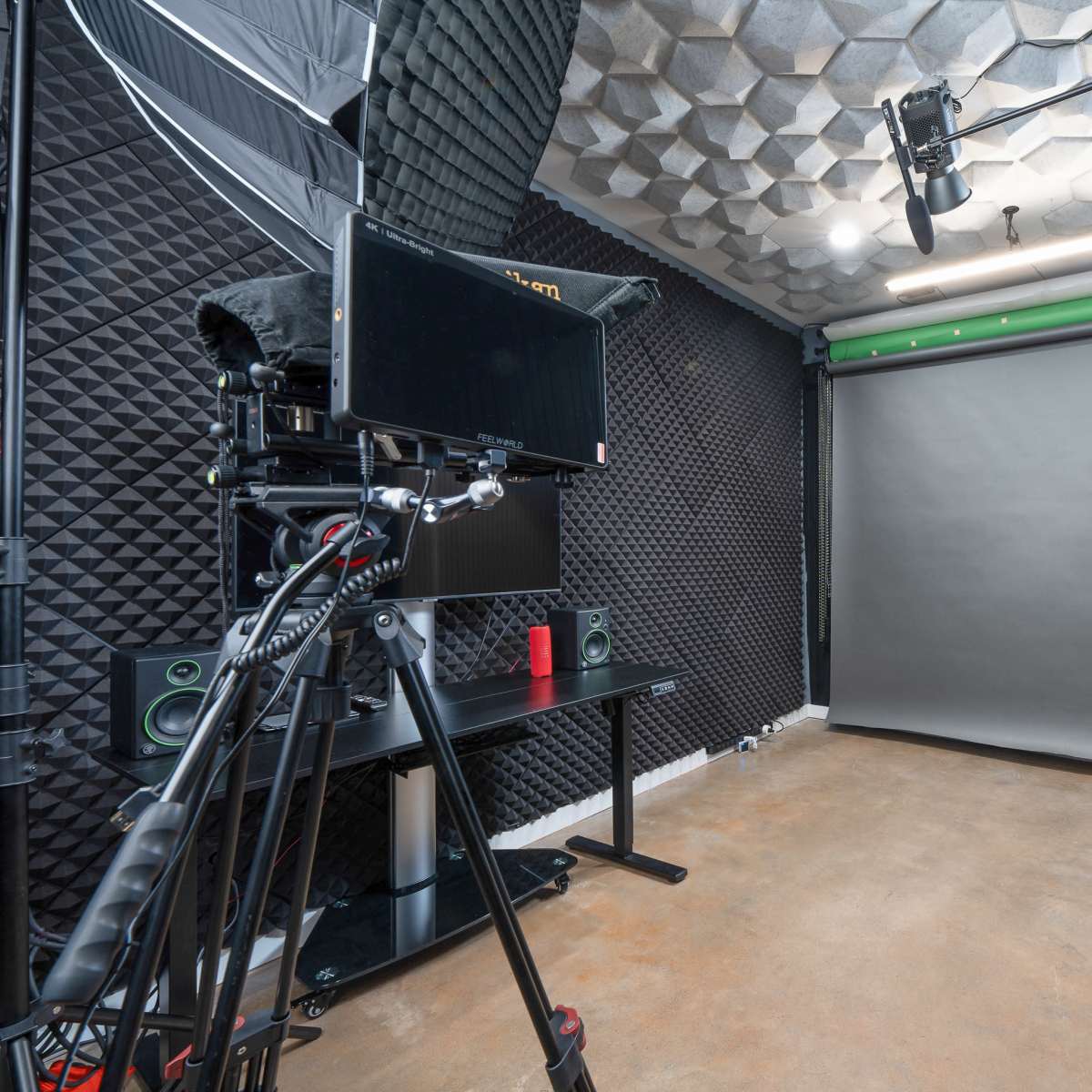 A photography studio equipped with a camera on a tripod, lighting fixtures, a green backdrop, and black acoustic paneling on the walls.