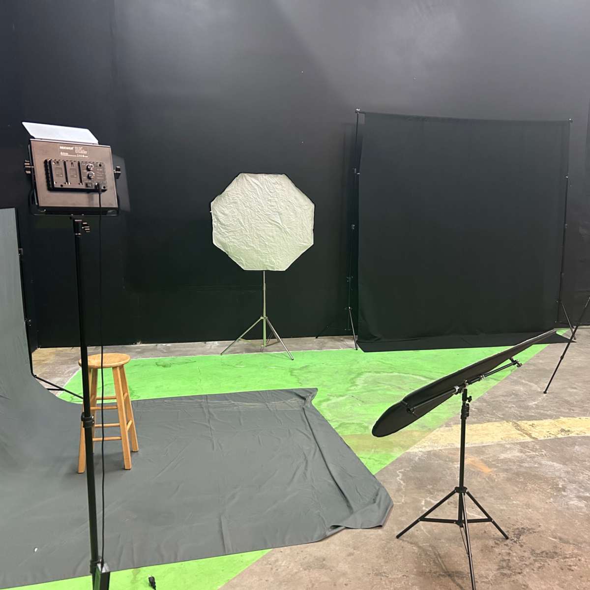 A photography studio with various backdrops, lighting equipment, and a stool on a green floor.