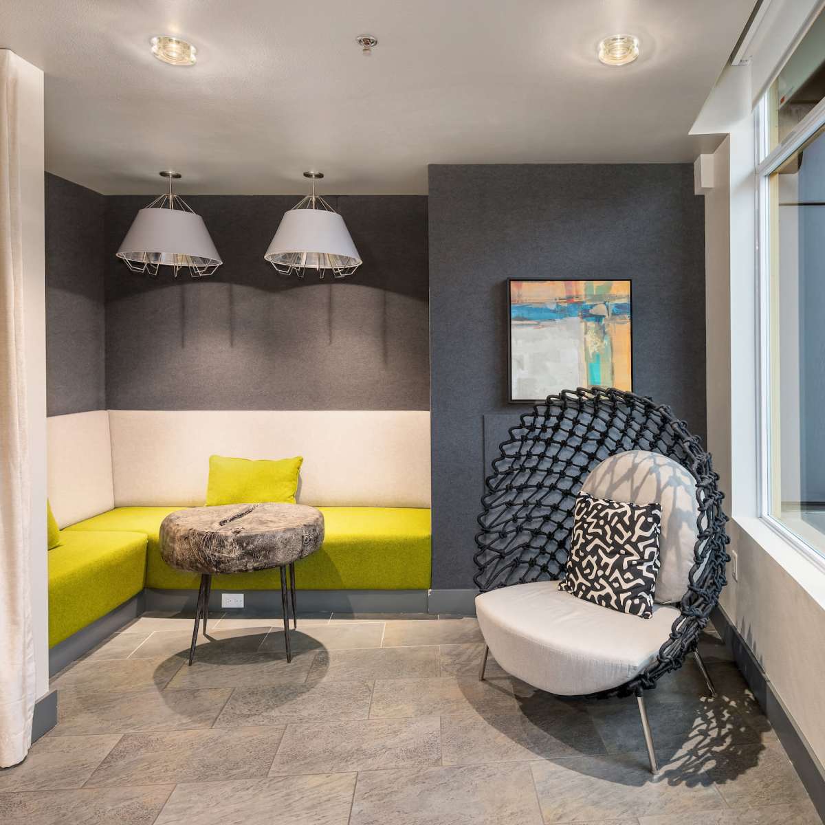A modern seating area with a curved green bench, a small table, and a large decorative chair positioned near a window.