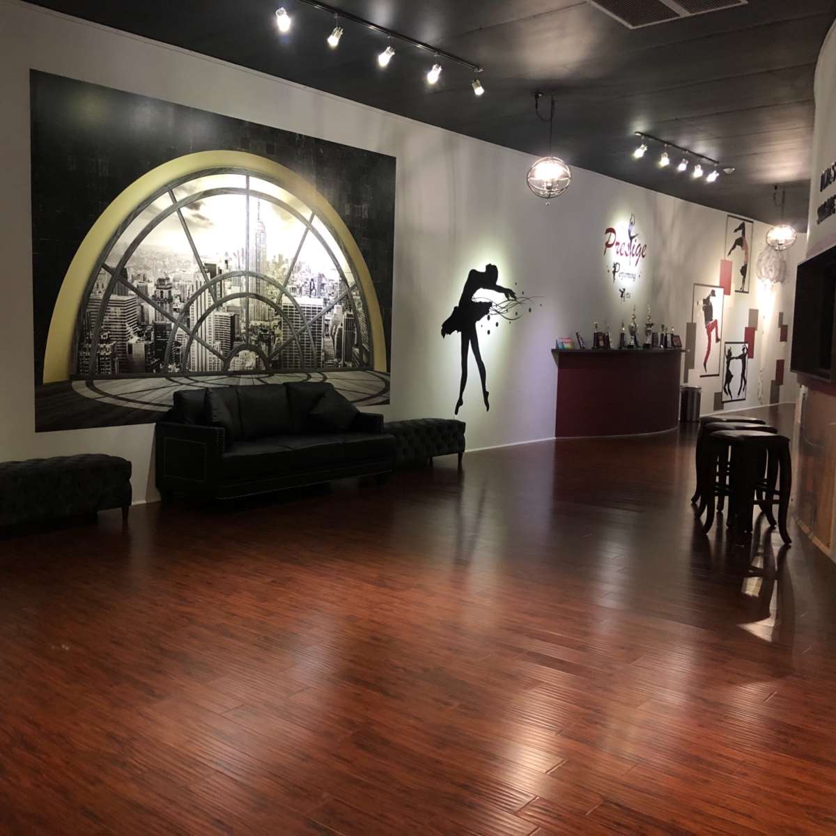 An interior space featuring a large mural of a cityscape, black and white silhouette artwork on the walls, a black sofa, and a bar area in the background.