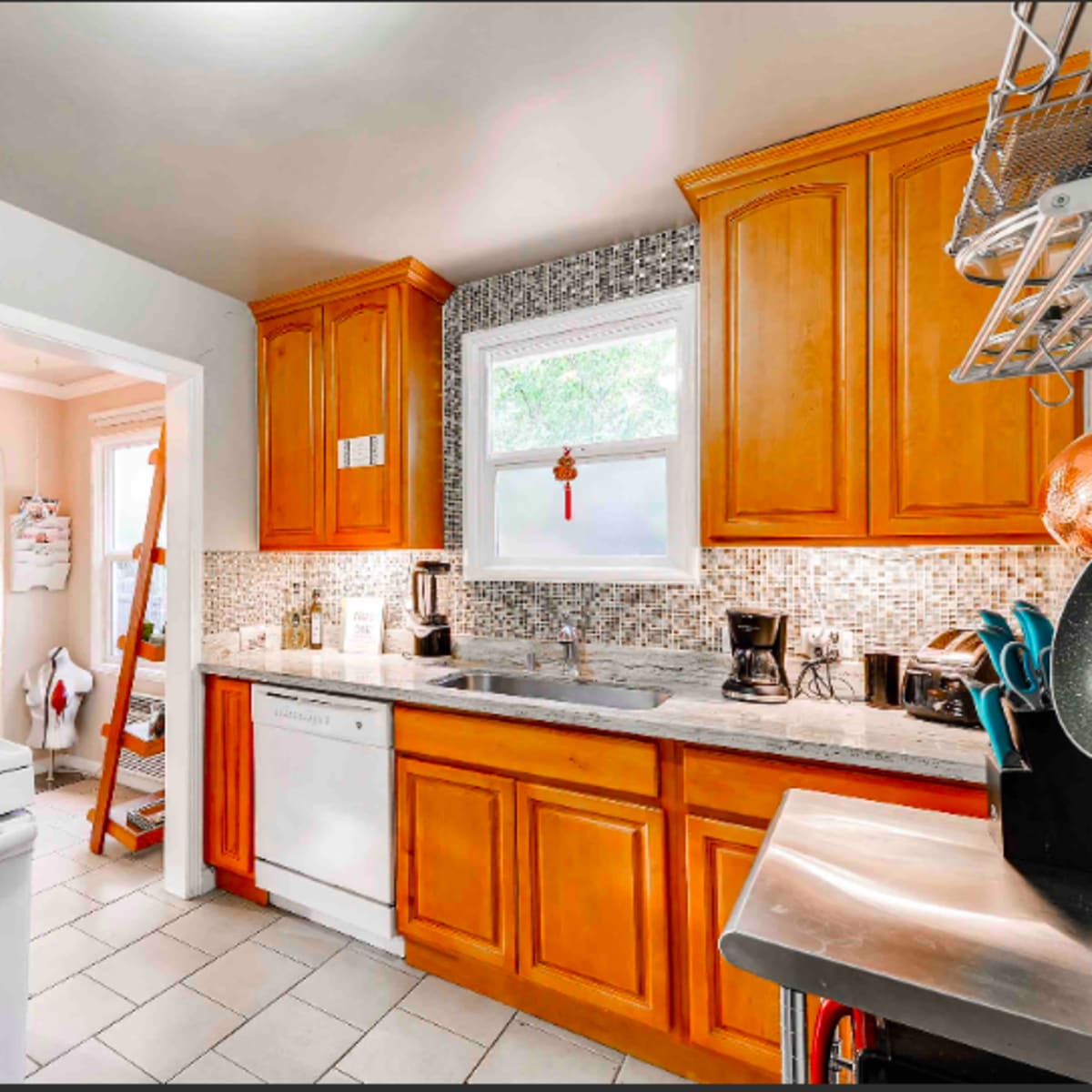 The kitchen features wooden cabinetry, a gas stove, a dishwasher, and a stainless steel countertop with mosaic tile backsplash.