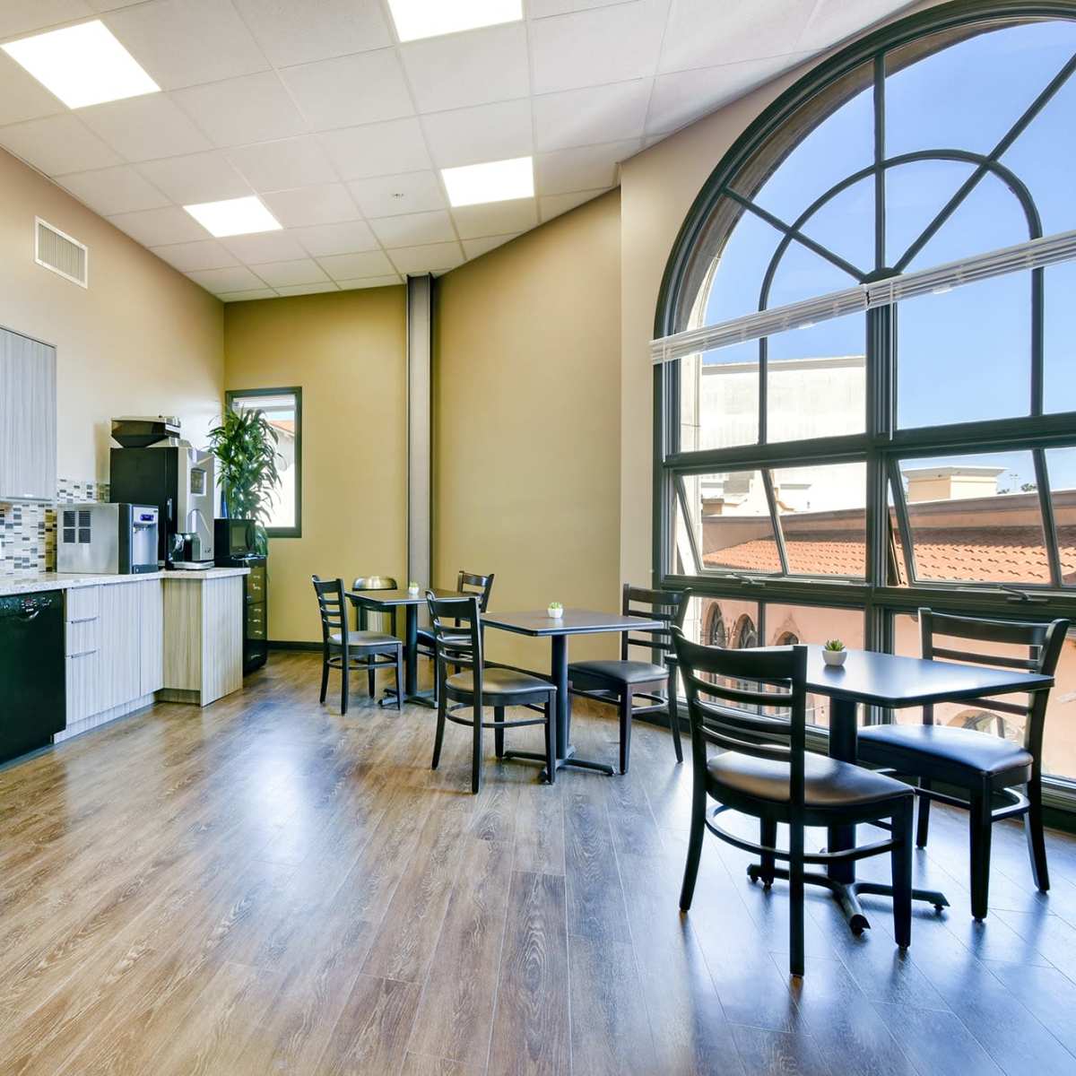 A modern kitchen area with wooden flooring, stainless steel appliances, and a dining space featuring a table and chairs by a large window.