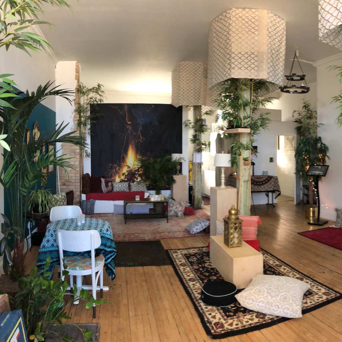 A spacious room filled with plants, decorative lamps, various seating arrangements, and artworks on the walls.