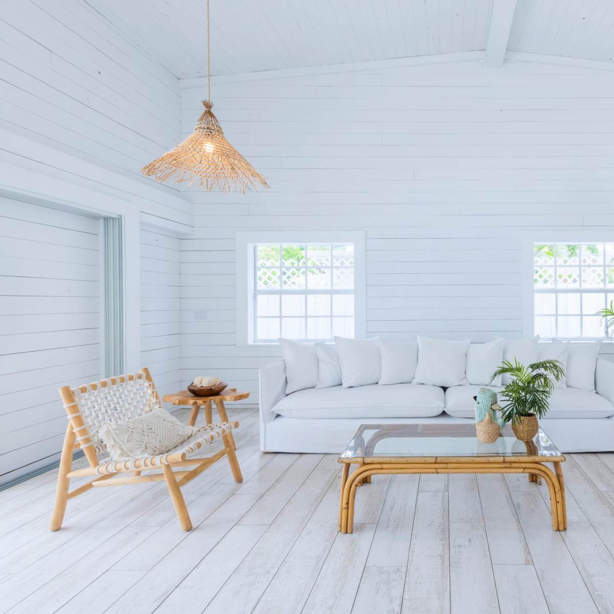 The scene features a minimalist living room with white walls, a white sofa, bamboo furniture, and natural light streaming through windows.