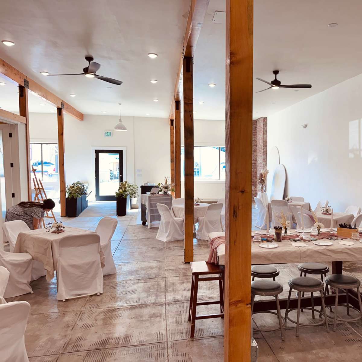 A spacious dining area with wooden beams, several tables set for a meal, and a minimalist decor style.