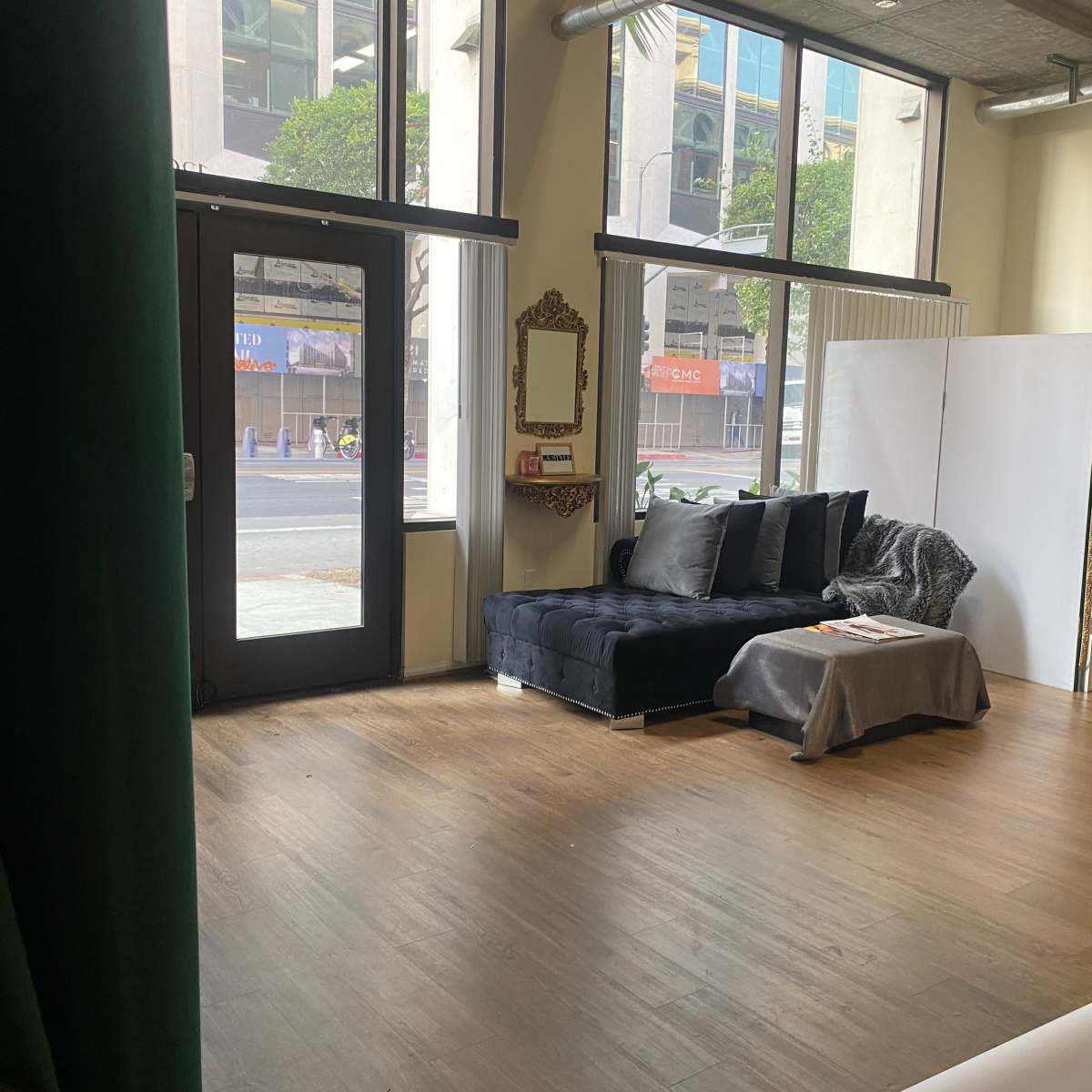 A stylish interior space with a dark couch, a large mirror, and a partition, all illuminated by natural light from large windows.
