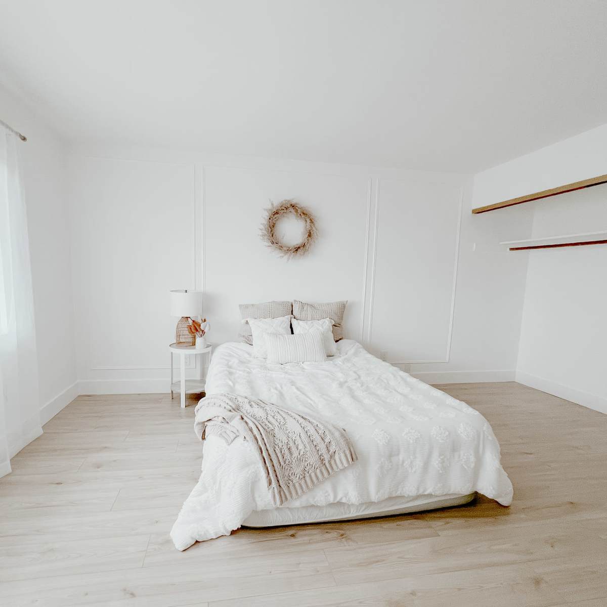 A minimalist bedroom featuring a bed with white bedding, a small bedside table, and a wall-mounted shelf.