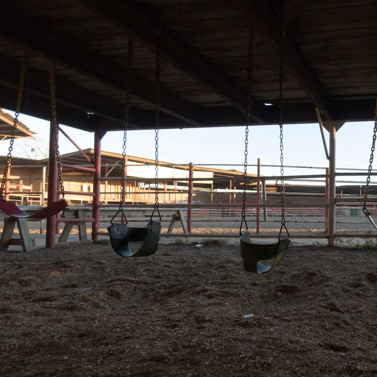 A row of swings hangs beneath a wooden structure in an empty playground area.