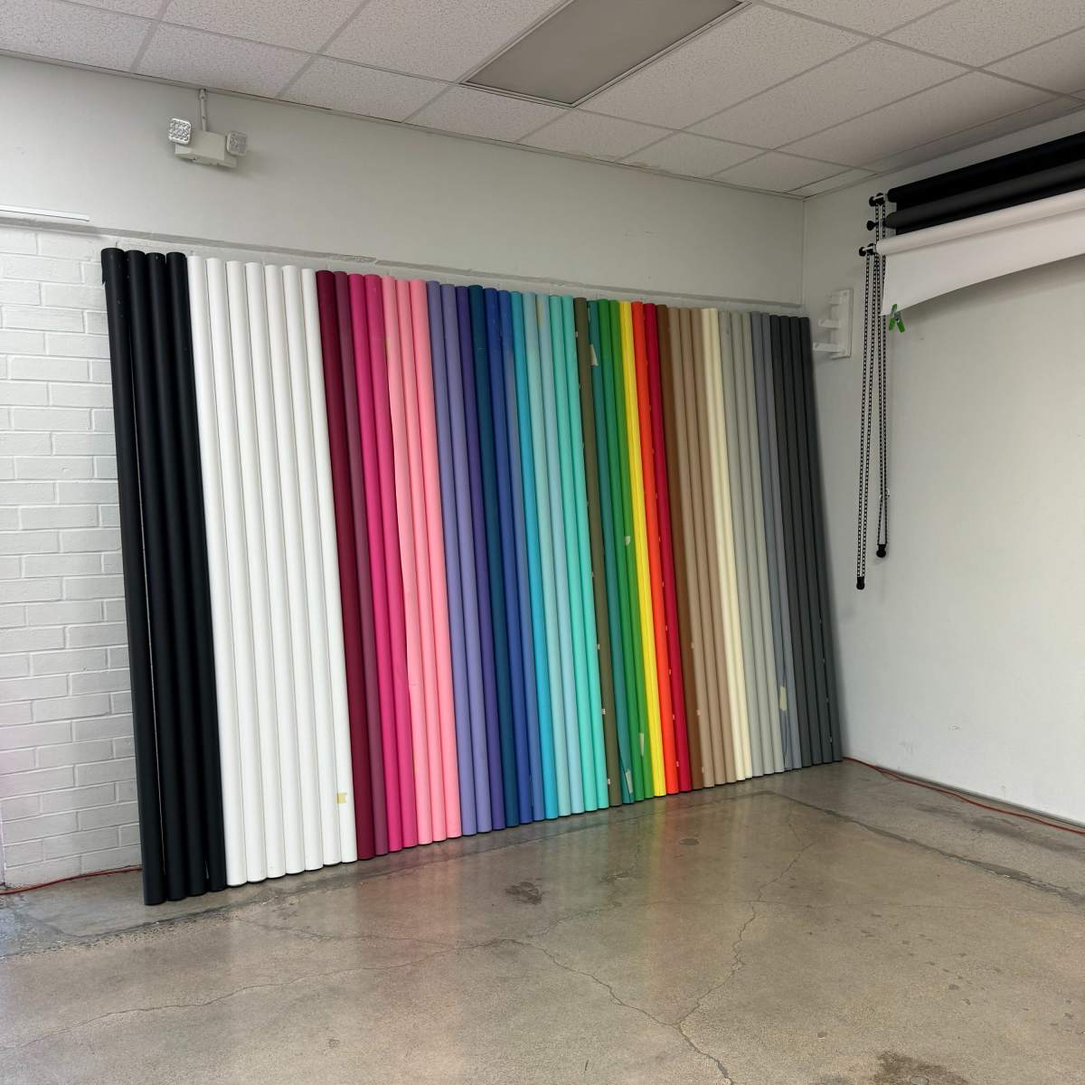 A wall displays a variety of rolled backdrops in multiple colors, arranged vertically in a studio setting.