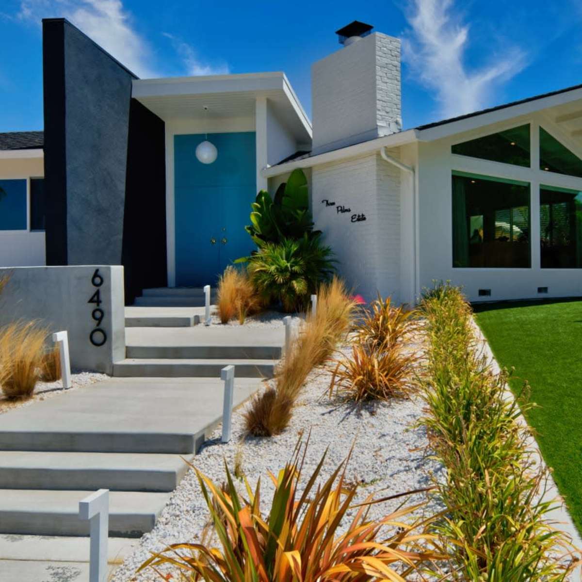A modern residential house with a mix of white and gray exterior, featuring a landscaped front yard with grasses and decorative rocks.