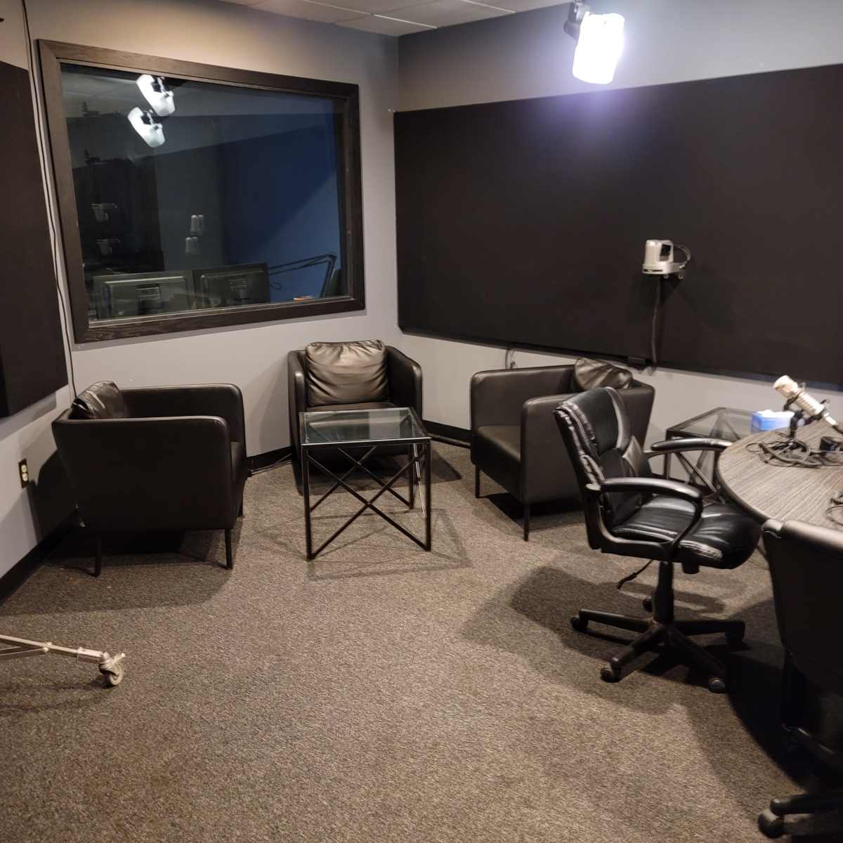 A small recording studio with two black chairs and a glass table arranged on a gray carpet.