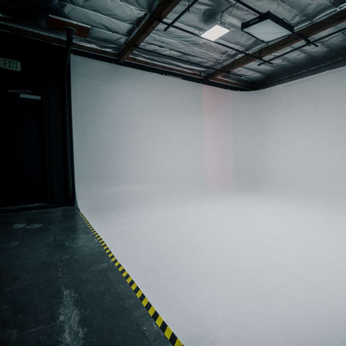A spacious, empty studio with a smooth white background and yellow caution tape along the floor.