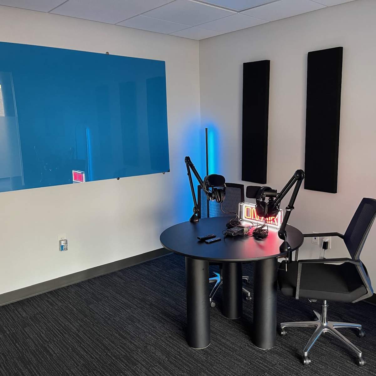 A small recording studio featuring a circular table with microphones, a chair, and sound-absorbing panels on the walls.