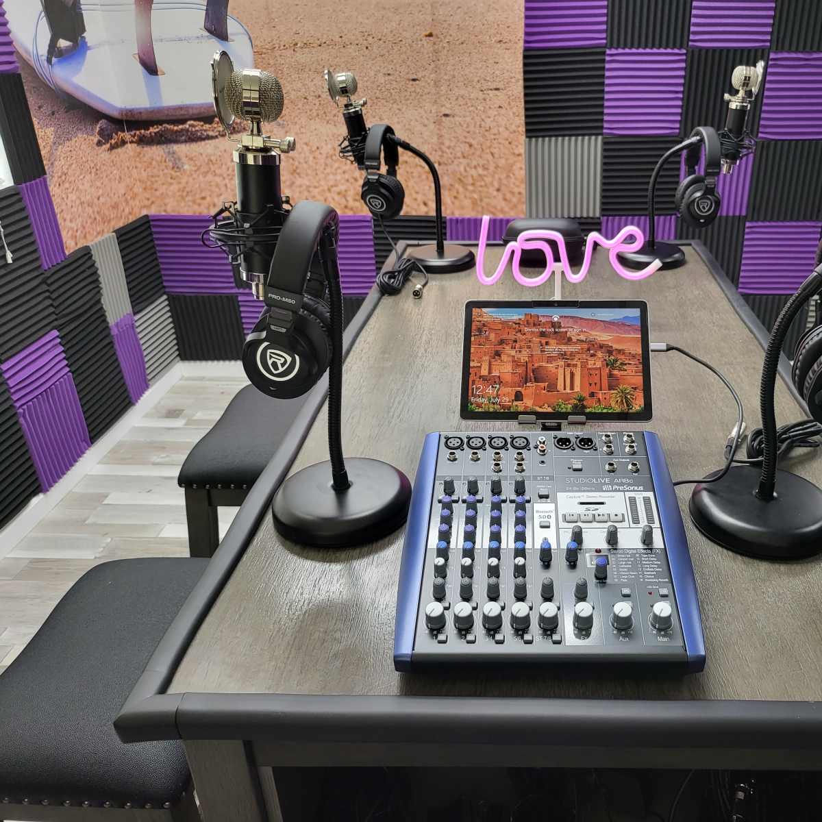 A recording studio setup with four microphones, headphones, a sound mixer, and a tablet displaying a scenic background on a table.