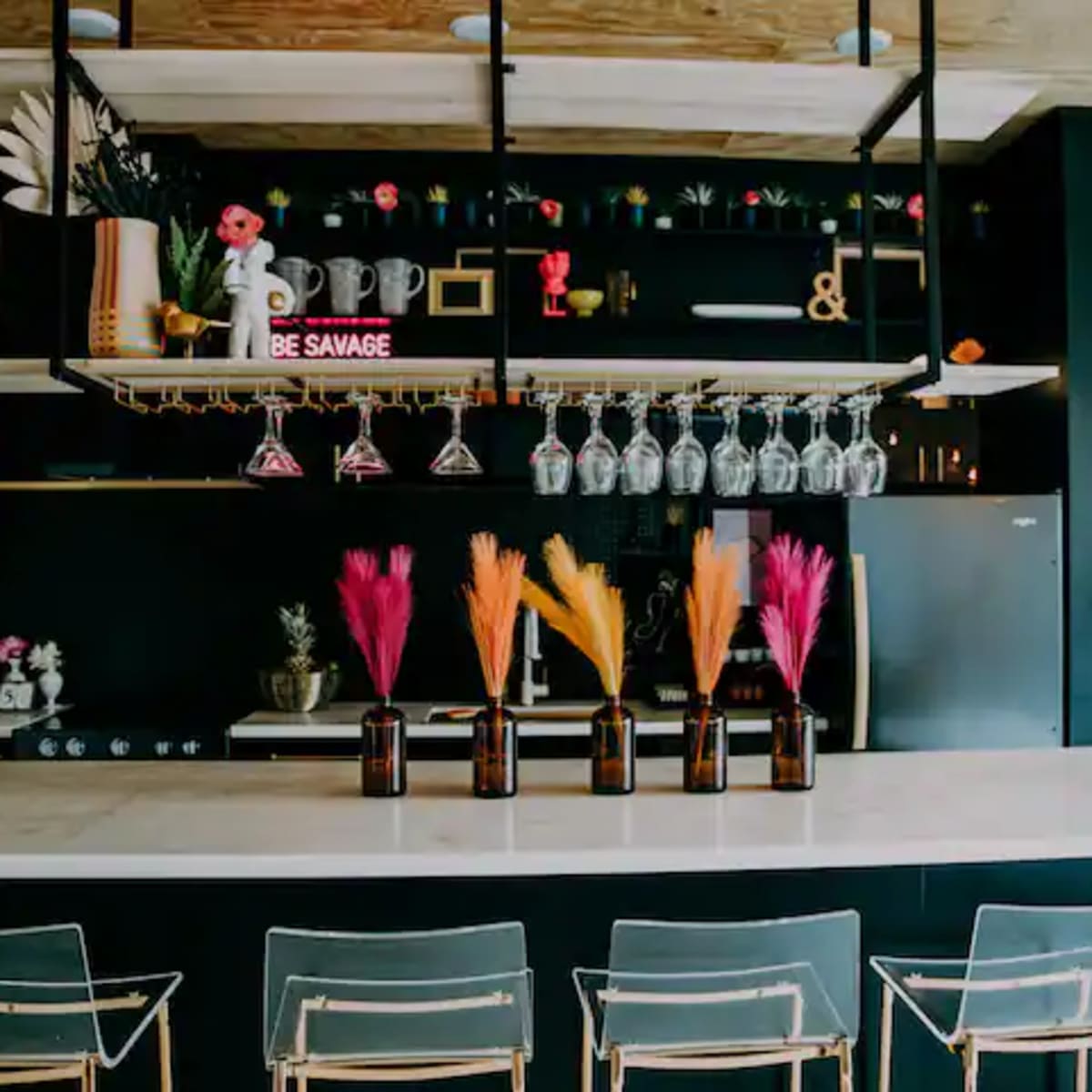 A modern bar with a black wall, a white countertop, and decorative plants in glass vases on display.