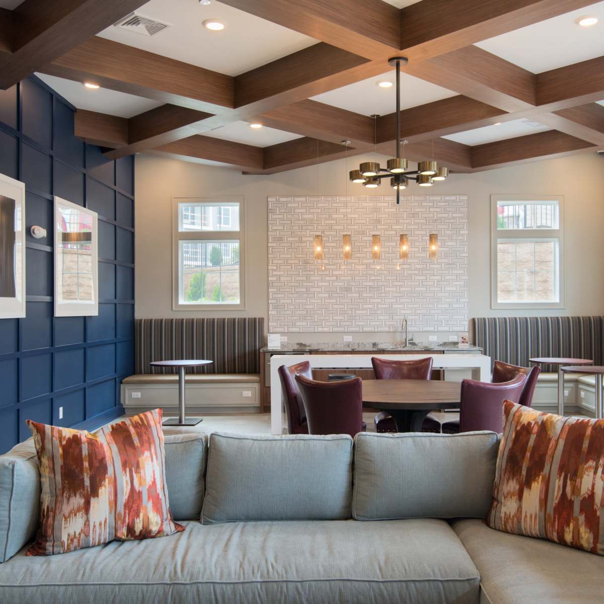 A modern lounge area with a blue accent wall, a coffered ceiling, and a mix of seating options, including a sofa with decorative pillows and dining tables.