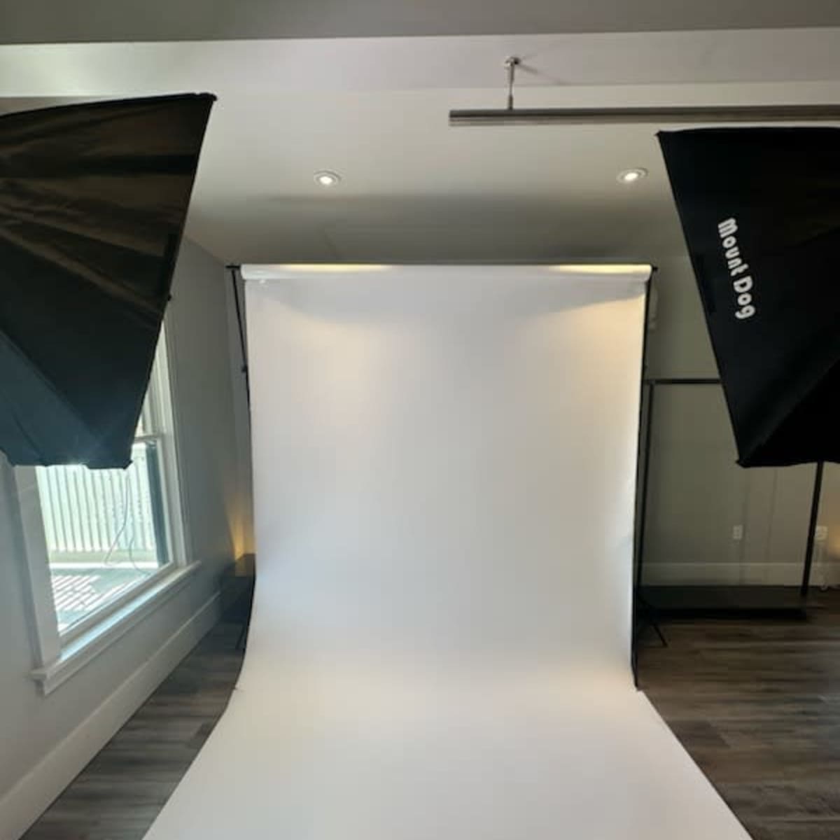 A photography studio setup featuring a white backdrop with two softbox lights on either side.