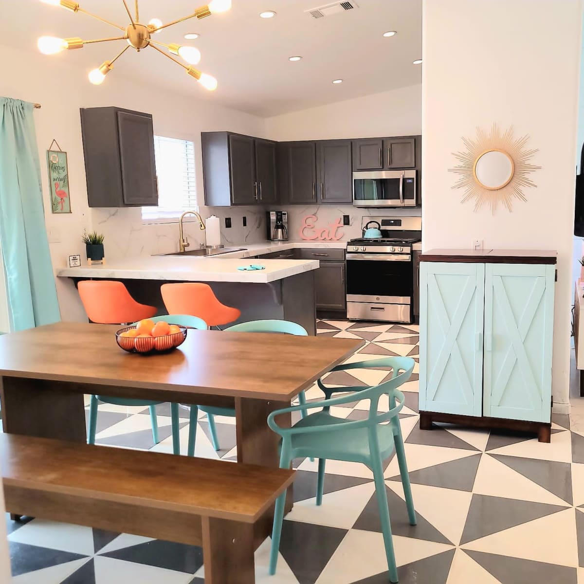 A modern kitchen and dining area featuring gray cabinetry, a wooden dining table, colorful chairs, and geometric patterned flooring.
