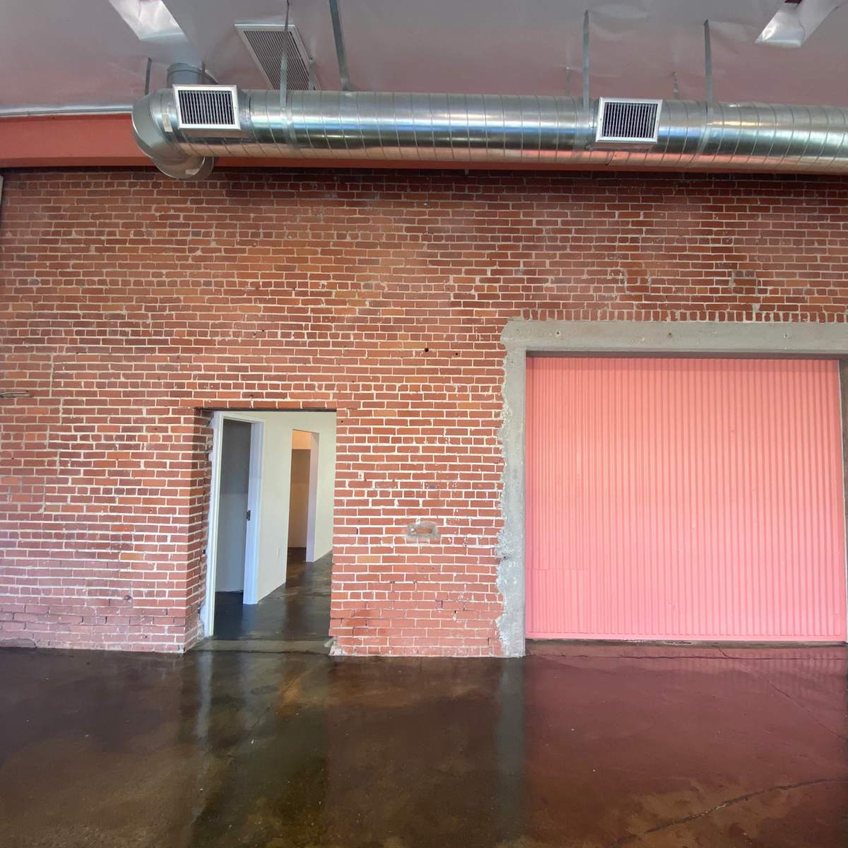 A brick wall with a pink roll-up door and an adjacent door opening in an industrial-style interior space.