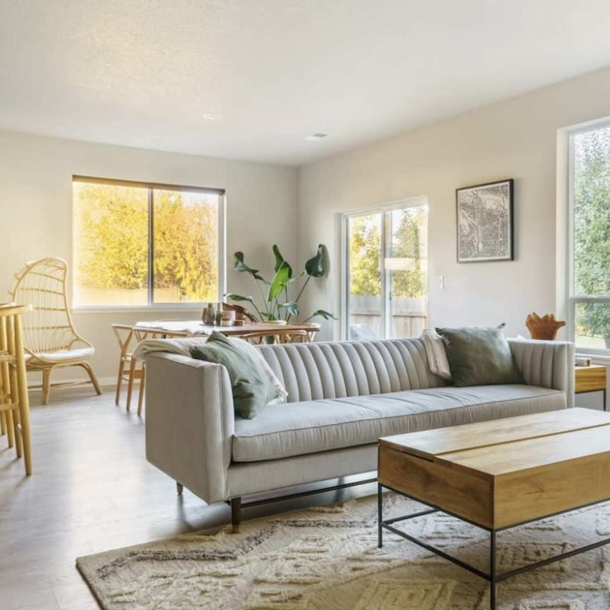 A modern living area features a striped sofa, a wooden coffee table, large windows, and a dining space connected to a kitchen.