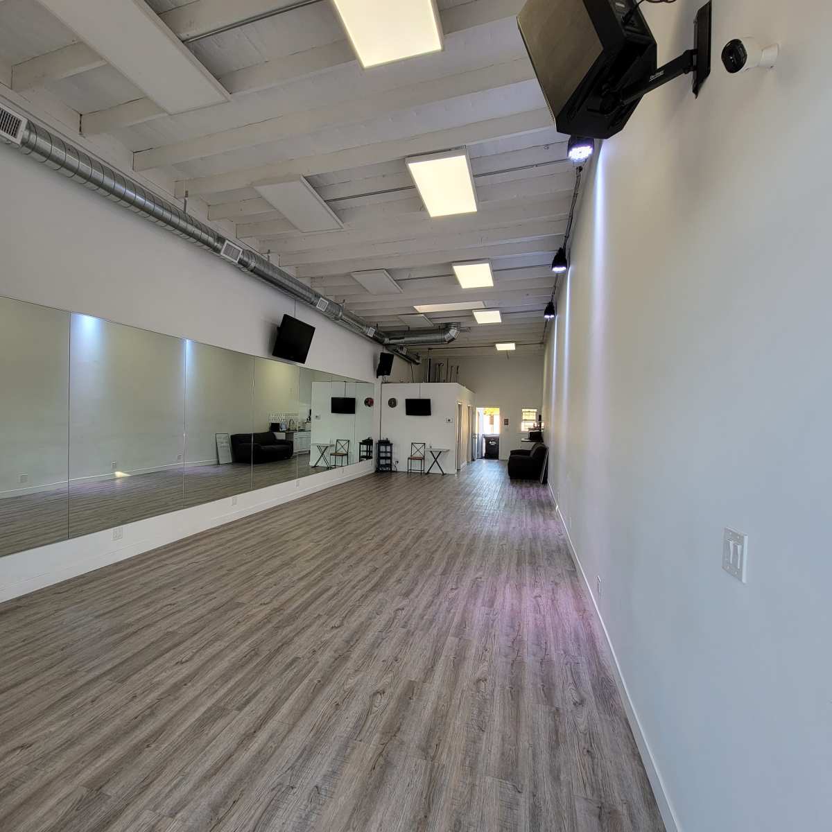 A spacious interior of a dance studio with wooden floors, bright lighting, and a large mirror along one wall.