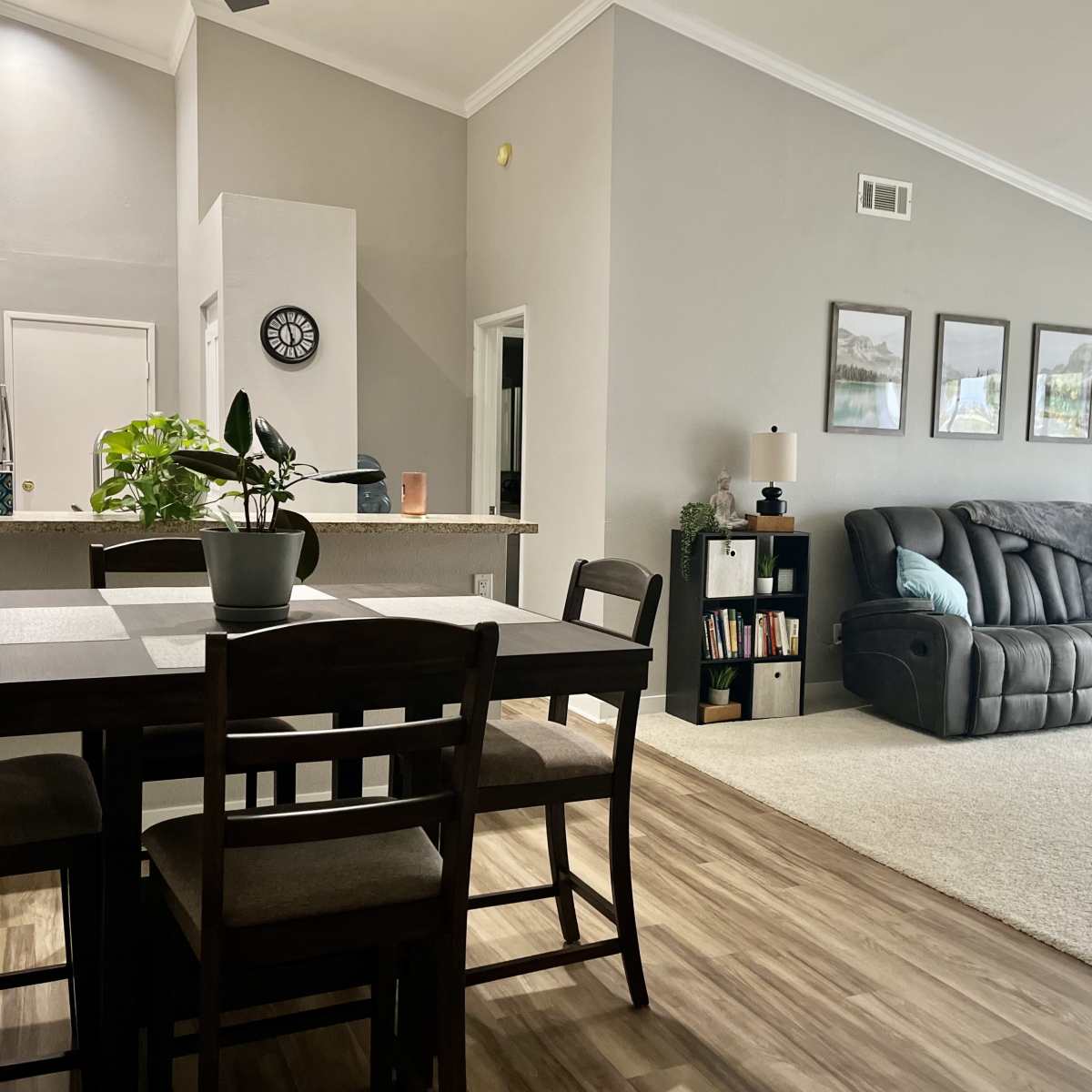 A spacious living area with a dining table, a gray sofa, and a large window, featuring neutral-colored walls and wood flooring.