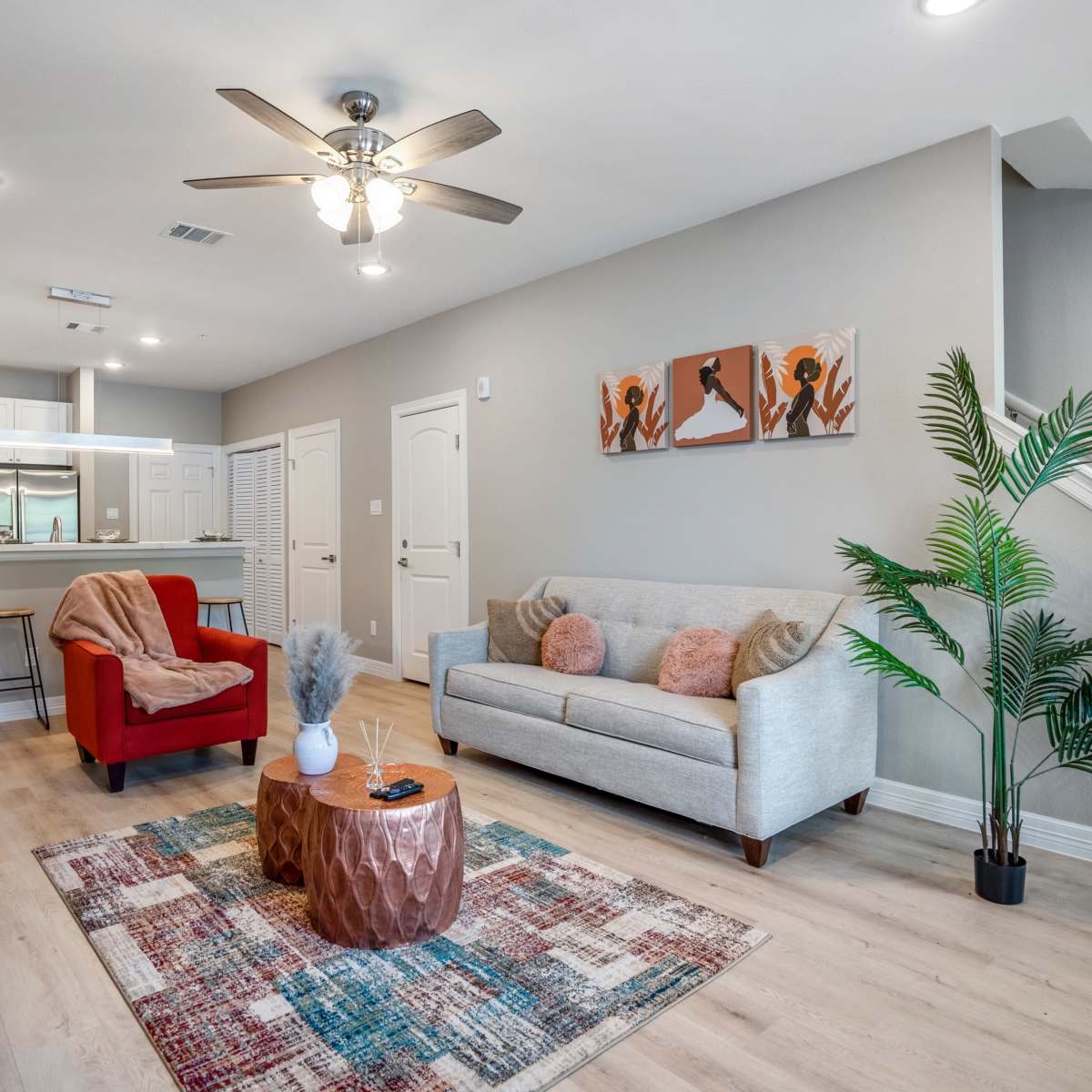 A modern living room with a light gray sofa, a red armchair, a circular coffee table, and a decorative plant, featuring a staircase and an open kitchen area in the background.