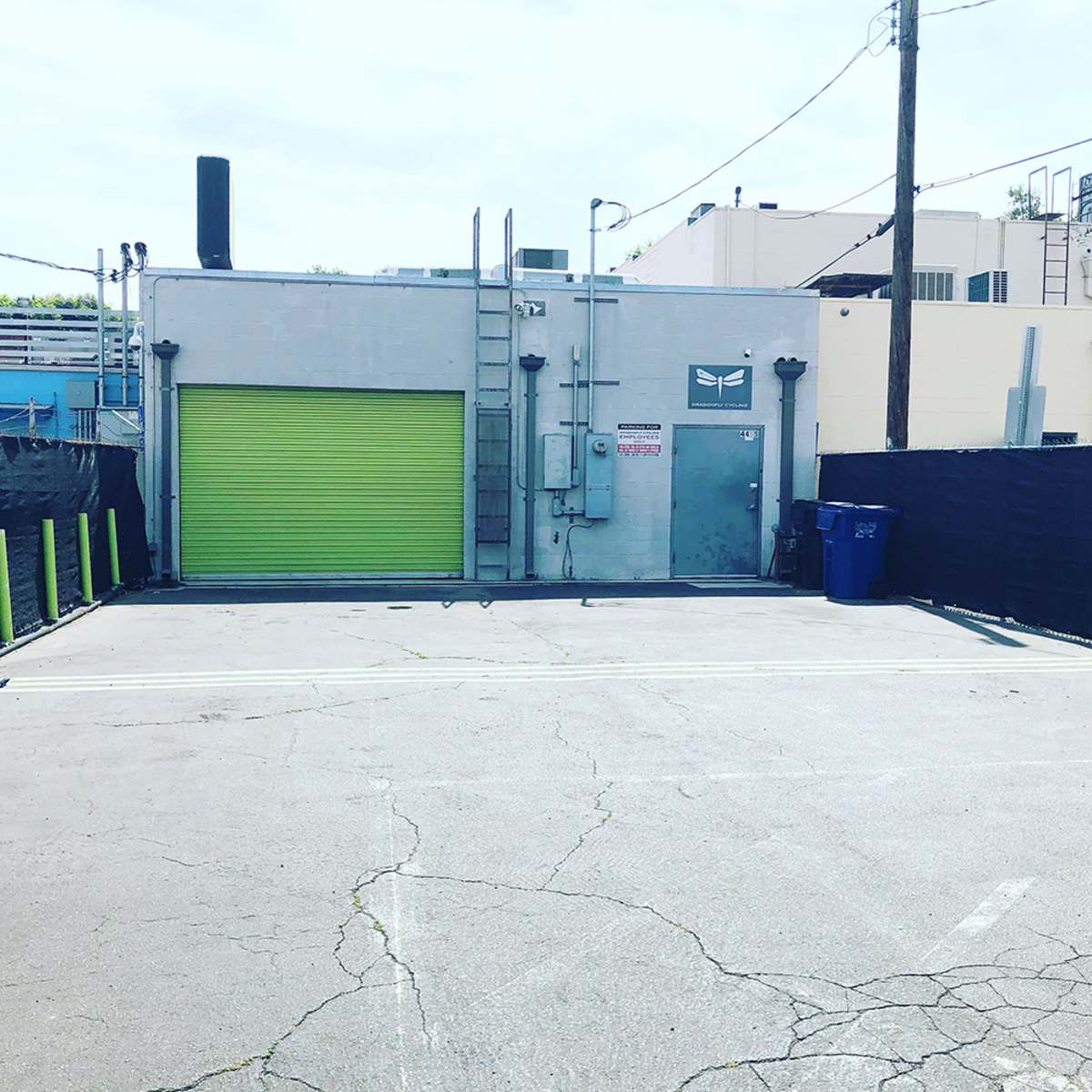 A gray building with a bright green garage door, flanked by trash bins and surrounded by a chain-link fence.