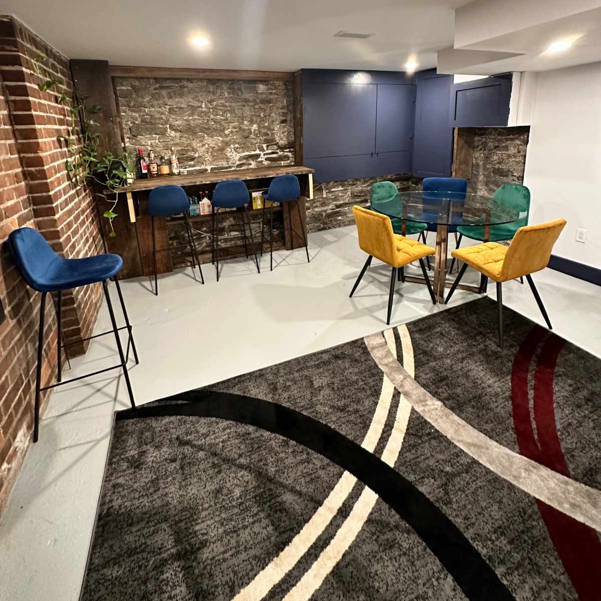 A modern basement bar area with a seating arrangement that includes colorful chairs and a stone wall backdrop.