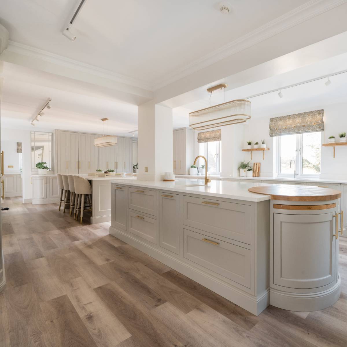 A modern kitchen with light gray cabinetry, an island with a wooden accent, and large windows allowing natural light to enter the space.
