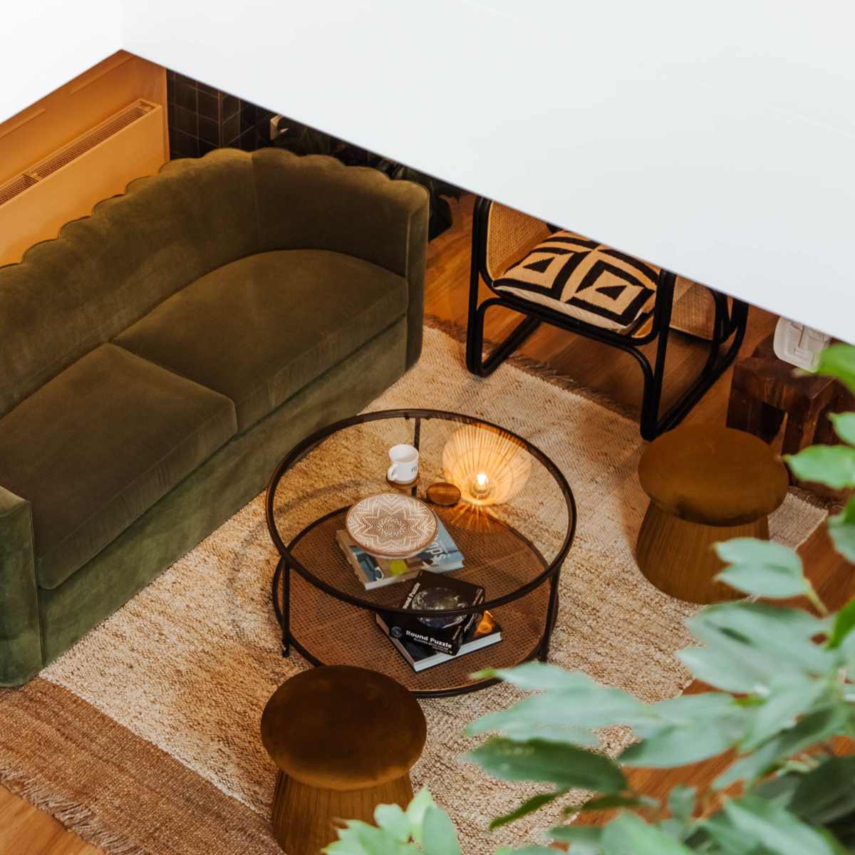 A cozy living room with a green scalloped sofa, a round coffee table, and several plants in the surrounding area.