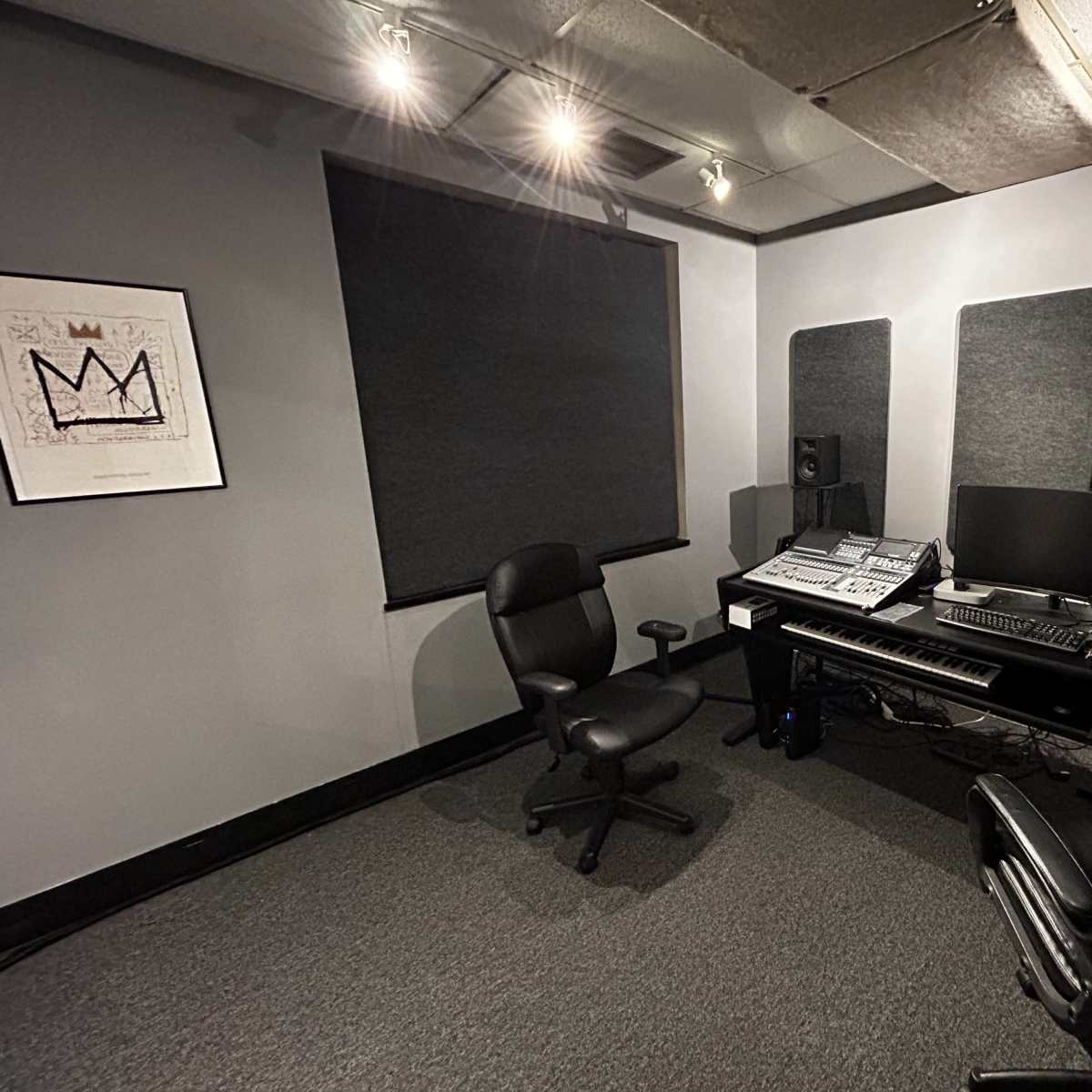 A music production studio with a desk, computer equipment, and soundproofing panels on the walls.