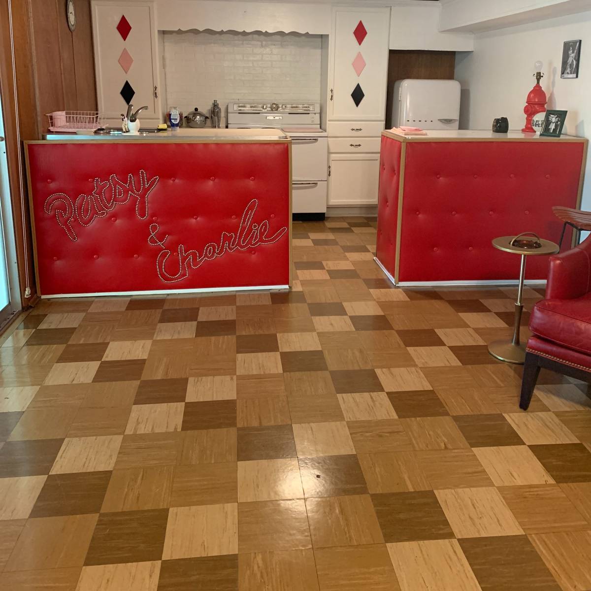 A retro-style kitchen with a red and white counter featuring the names "Patsy & Charlie," surrounded by a checkered wood floor.