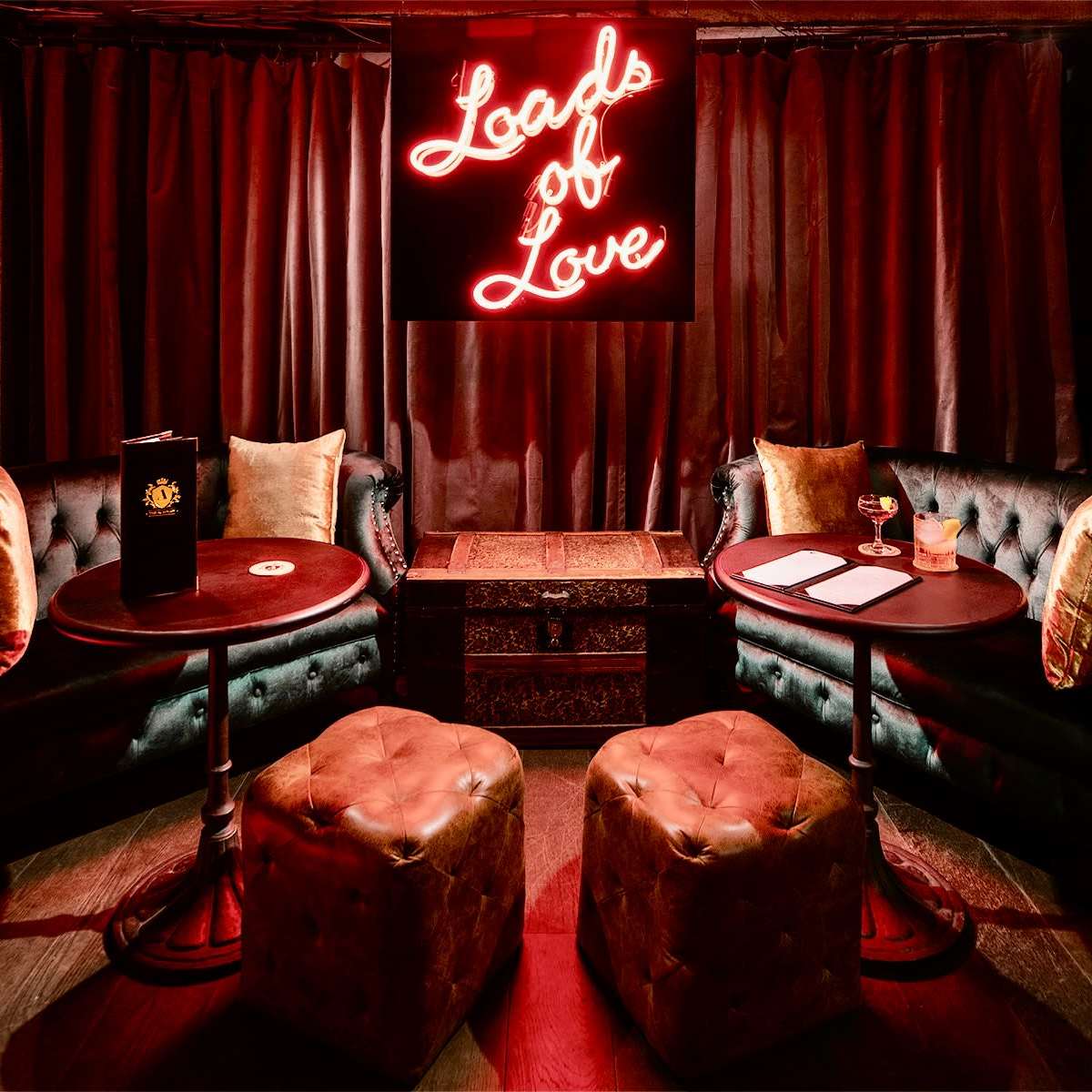 A cozy lounge features dark curtains, plush velvet seating, and a neon sign that reads "Loads of Love."