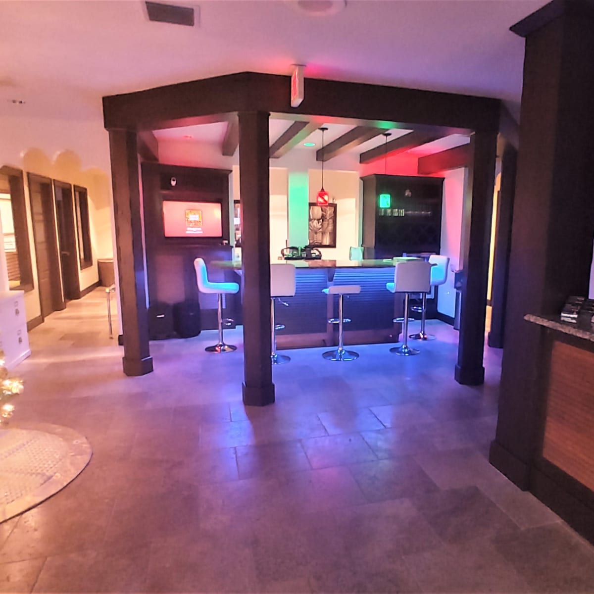 The scene features a spacious, modern room with a decorated Christmas tree on one side, a bar area with illuminated seats, and vibrant colored lighting throughout.