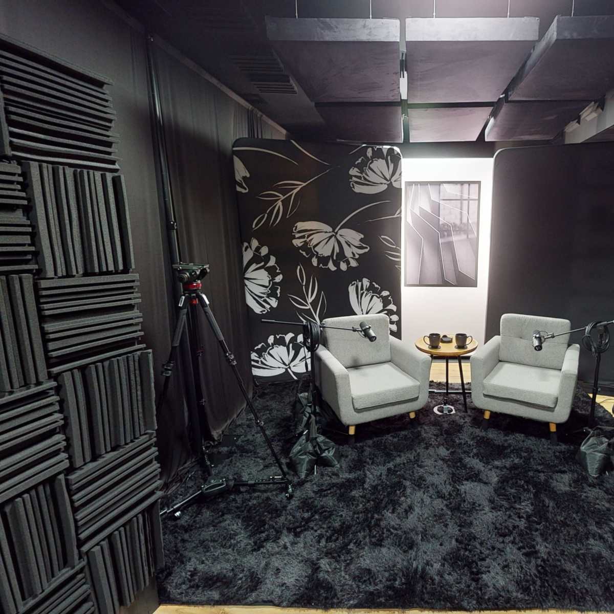 A soundproof studio setup with two gray chairs, a small table, and black acoustic panels on the walls and floor.