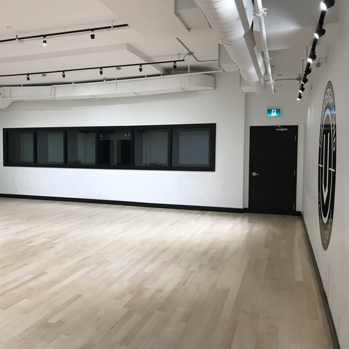 A spacious dance studio with wooden flooring, large windows, and a mirror along one wall.