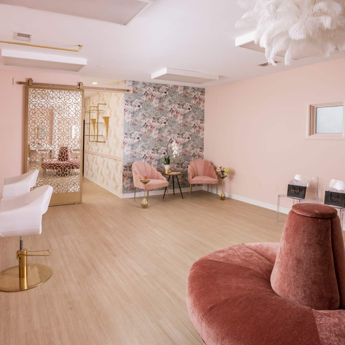A modern, light-colored salon interior with floral wallpaper, pink accents, and stylish seating arrangements.