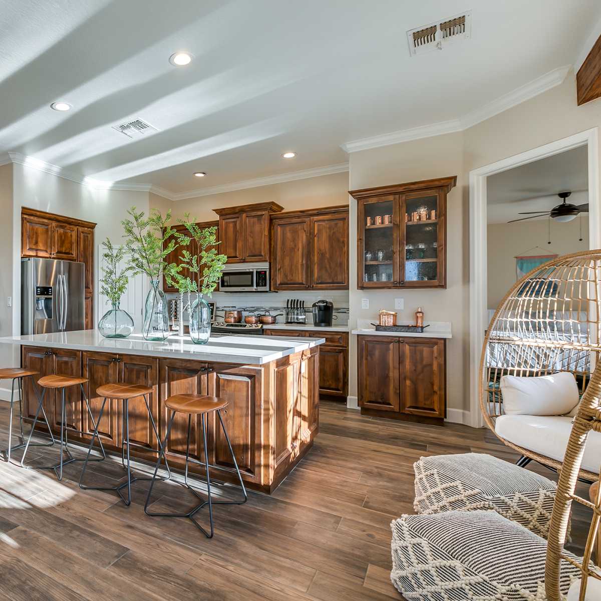 A modern kitchen features wooden cabinets, a large island with bar seating, and natural light streaming through the windows.