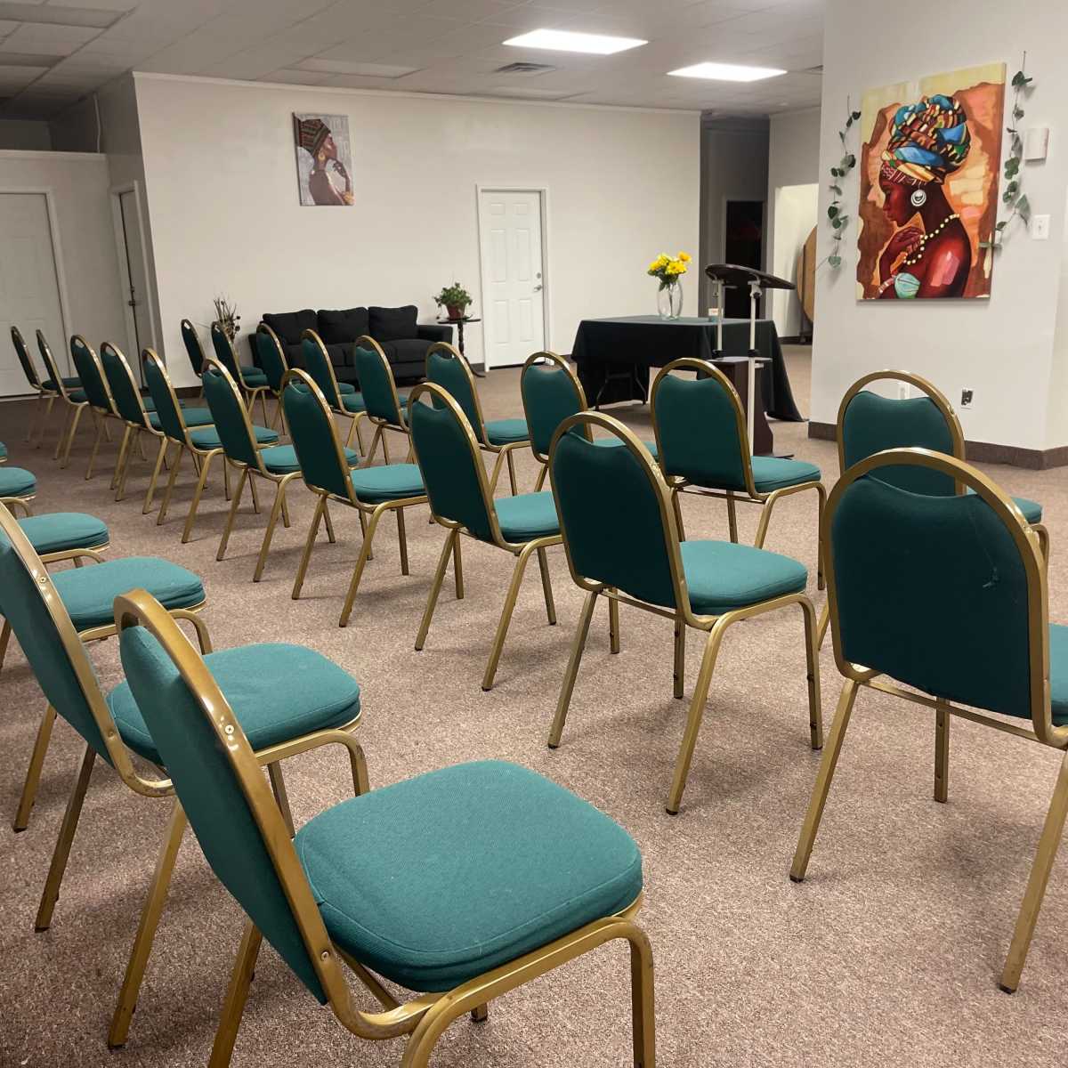 A room arranged with neatly aligned green chairs facing a small stage with a black table and flowers.