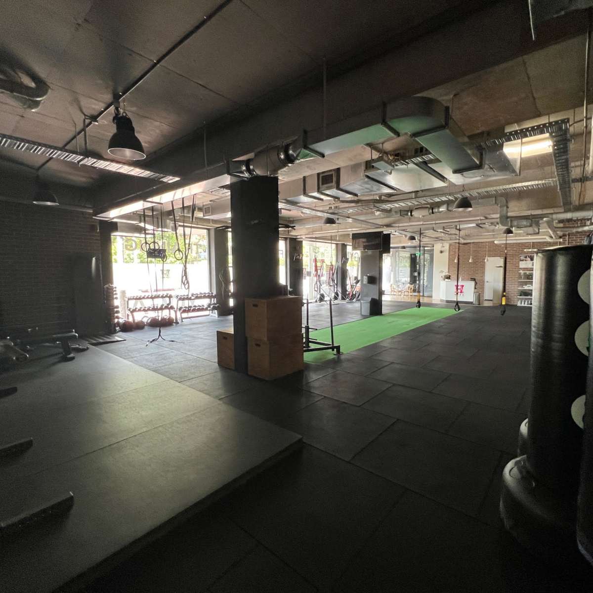 A spacious gym with exercise equipment, including punching bags and fitness mats, under industrial-style lighting.