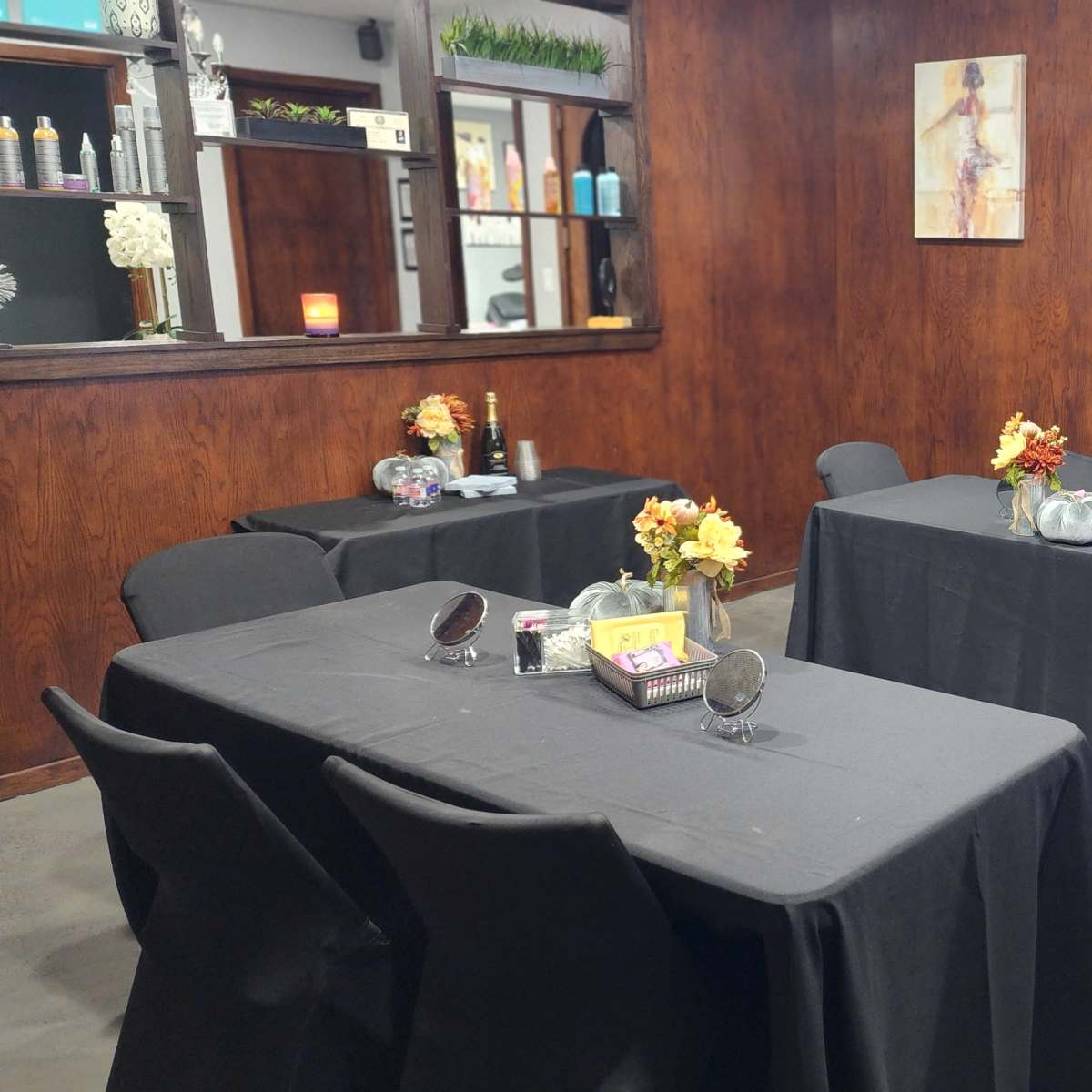 A dimly lit salon room with several covered tables decorated with vases of flowers and mirrors.