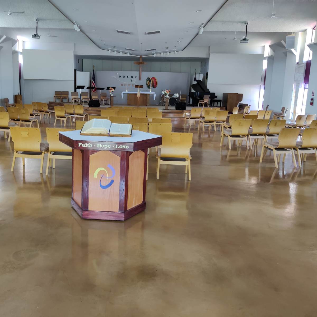 The interior of a church features a central altar surrounded by rows of wooden chairs and various religious symbols.